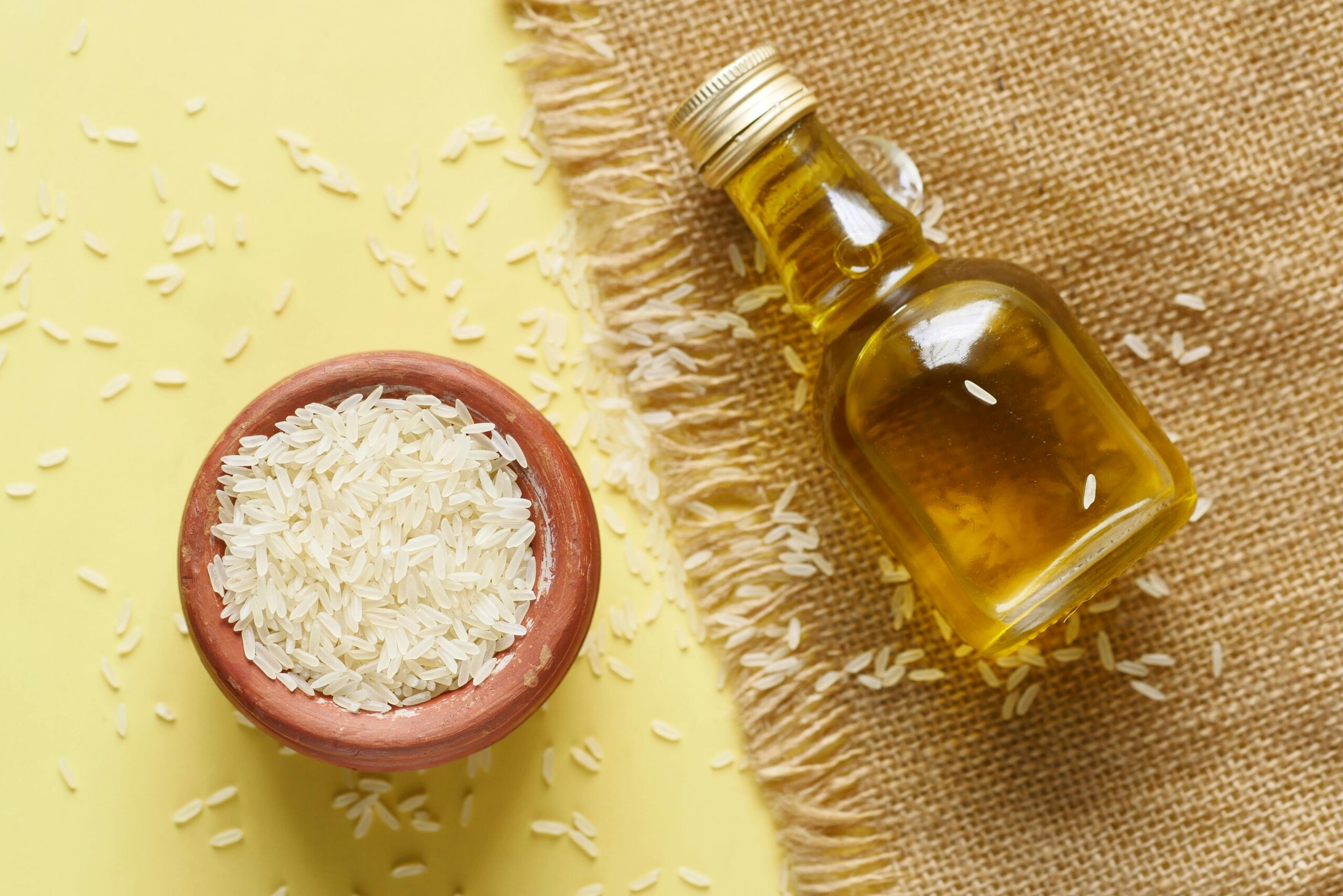 Close-up of rice in a ceramic bowl with a bottle of oil on a burlap background.